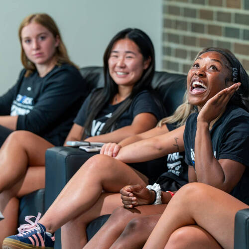 student athletes in black t-shirts sit in black chairs during a panel discussion
